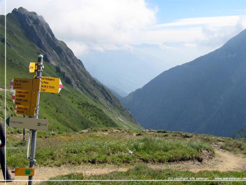TMB. P grnsen mellem Frankrig og Schweiz str et skiltetr, hvor et af skiltene er mrket med det rd/hvide TMB mrke og viser 3 timer til Trient
